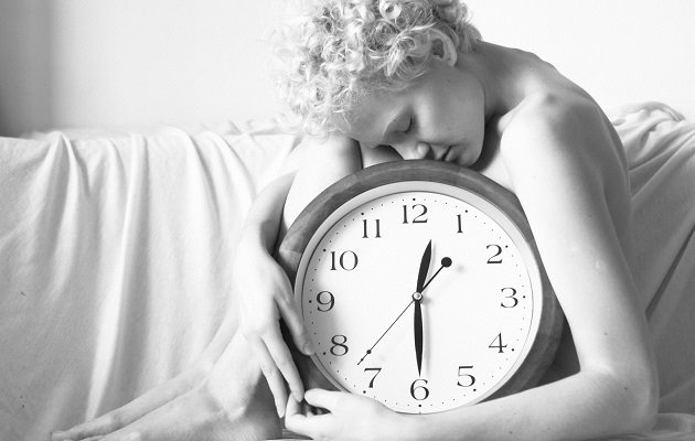 Женщина сидит возле кровати и держит в руках часы